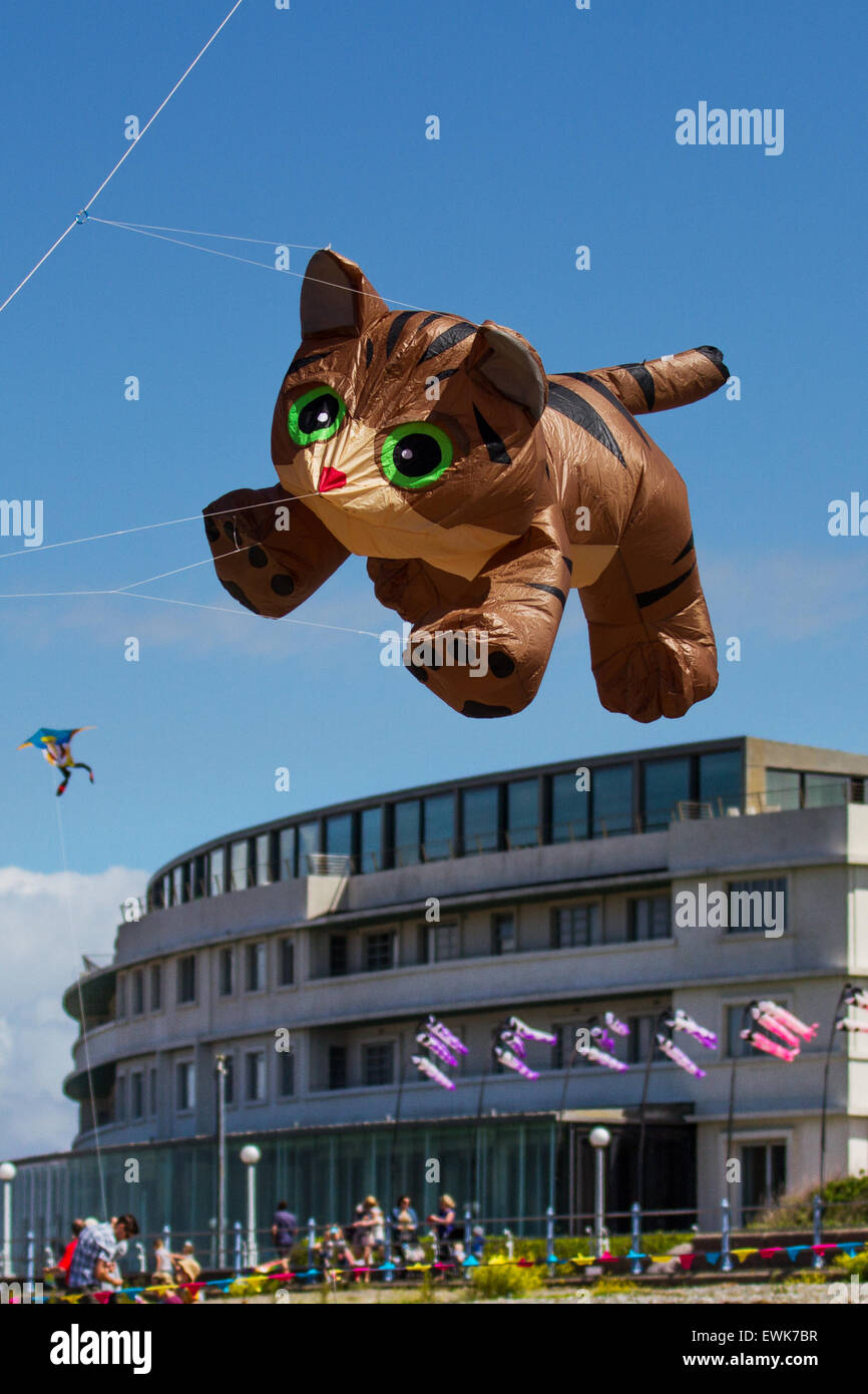 Morecambe, Lancashire, UK 27th June, 2015. Catch The Wind Kite Festival an annual festival on Morecambe seafront, when for the whole day the skies are full of the most spectacular shapes, colours and pussycat animal creations. Featured were single line show kites of all kinds and sizes, including a massive 40 feet tall long large inflatable brown Cat guaranteed to scare the heck out of any animals on the beach, seen here flying over the Midland Hotel. Stock Photo