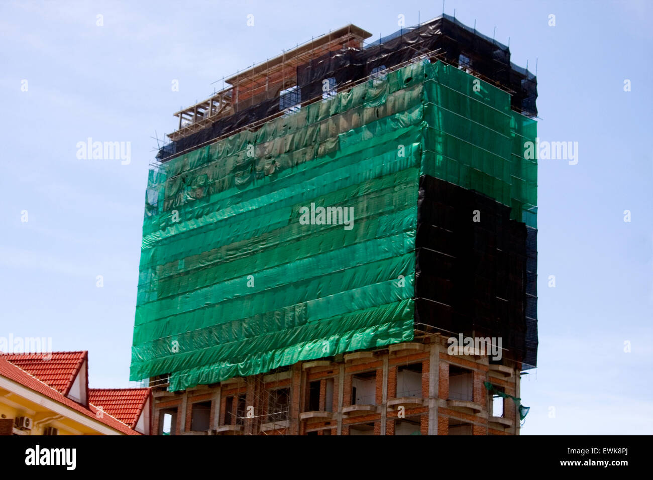 A new highrise cement & brick building is covered with a green tarp above a city street in Kampong Cham, Cambodia. Stock Photo