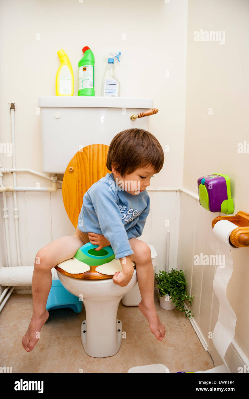 Caucasian child, boy, 4-5 year old, sitting on child toilet seat and unraveling toilet roll on holder all over the floor, that Andrex moment. Stock Photo