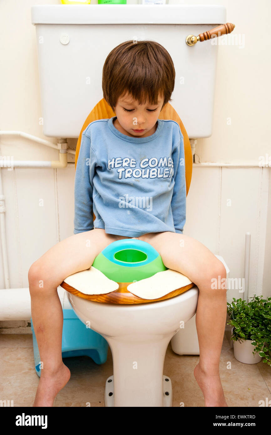 Caucasian young child, boy, 4-5 year old, facing viewer, sitting on baby seat on top of toilet during toilet training. Looking down between his legs. Stock Photo