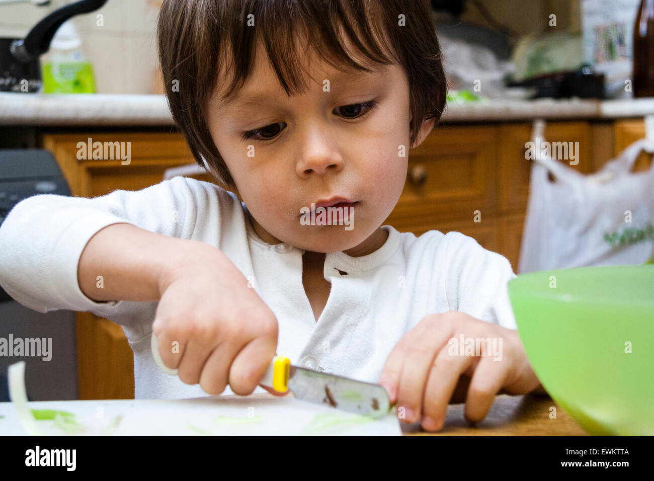 Caucasian child, boy, 45 year old, sitting indoors at kitchen table and cutting up food with a