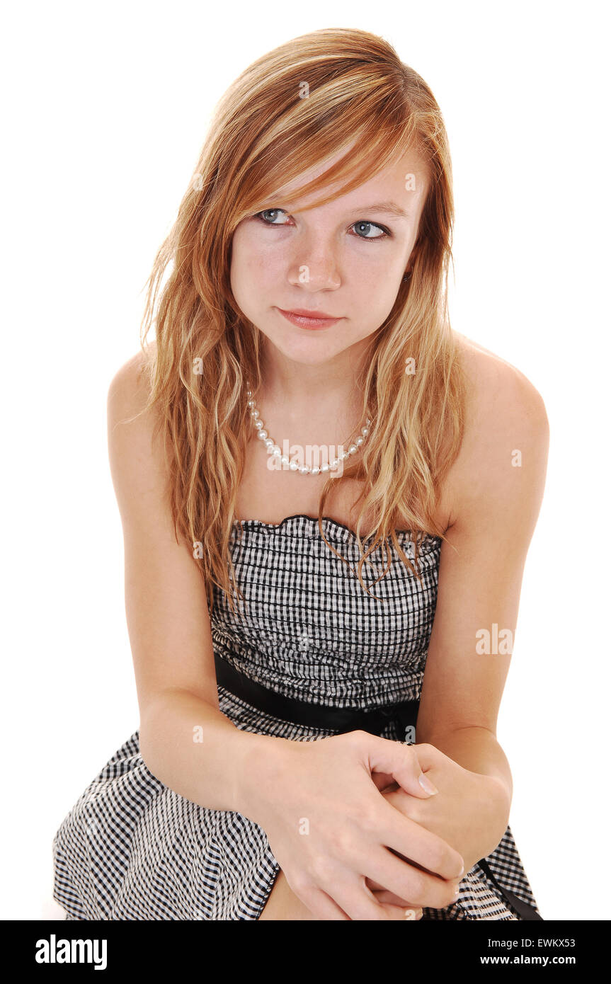 A young pretty blond woman in a black white dress and black heels, sitting in the studio on the floor, over white background. Stock Photo
