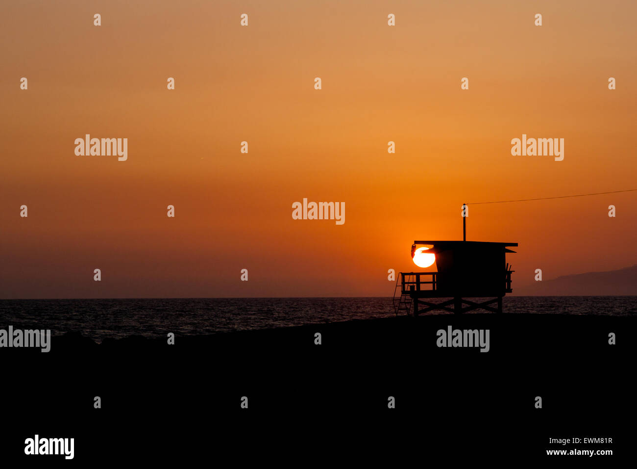 An orange California sun sets behind a lifeguard tower in Venice Beach. Stock Photo