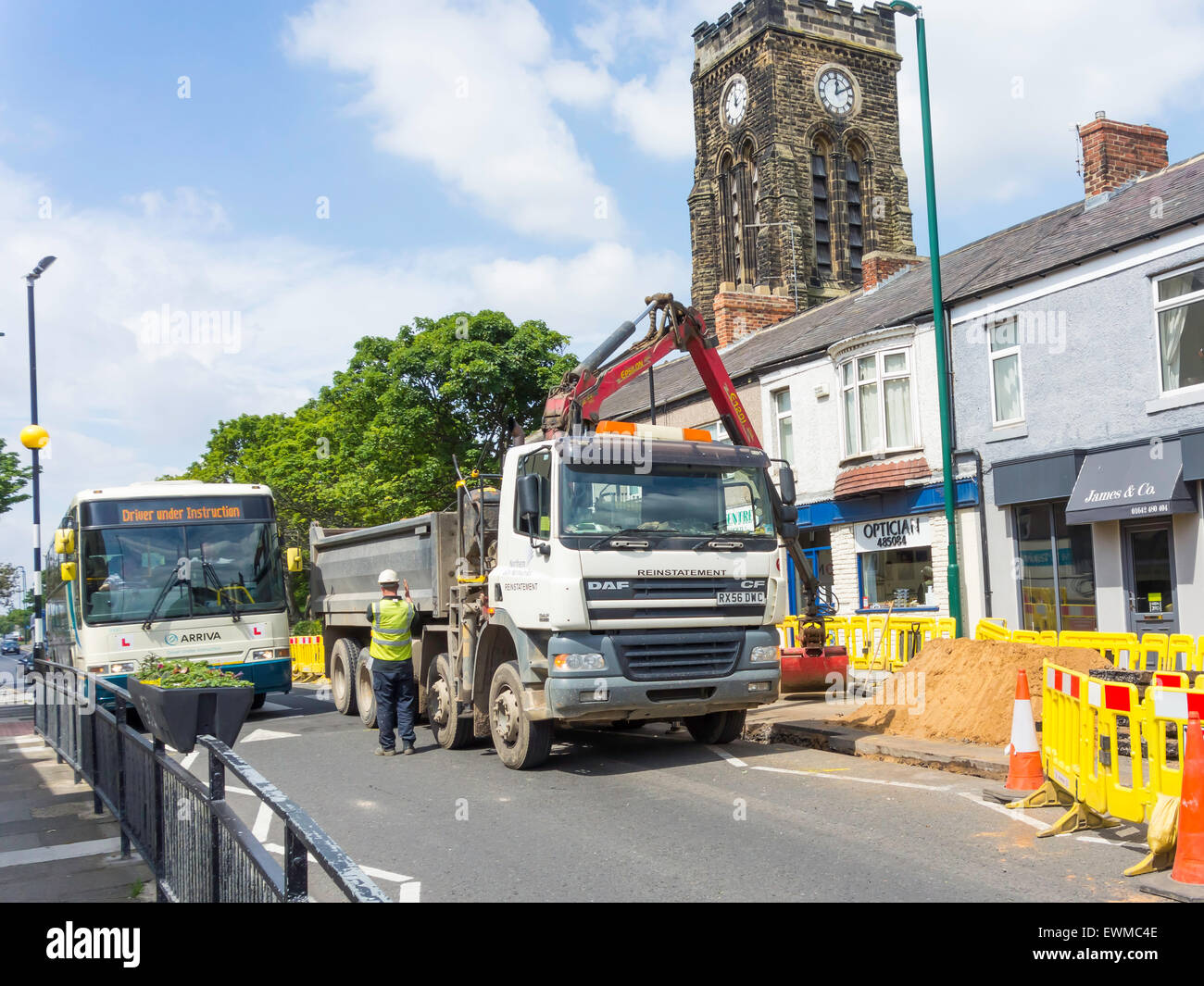 A bus being guided through a narrow gap while road narrowed for gas main replacement works in Marske Village Centre Stock Photo
