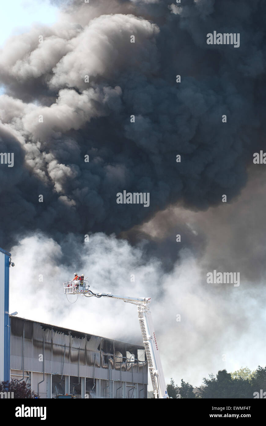 Firemen on aerial ladder platform in front of big cloud of smoke, Industrial Area Melbeck, Lower Saxony, Germany Stock Photo