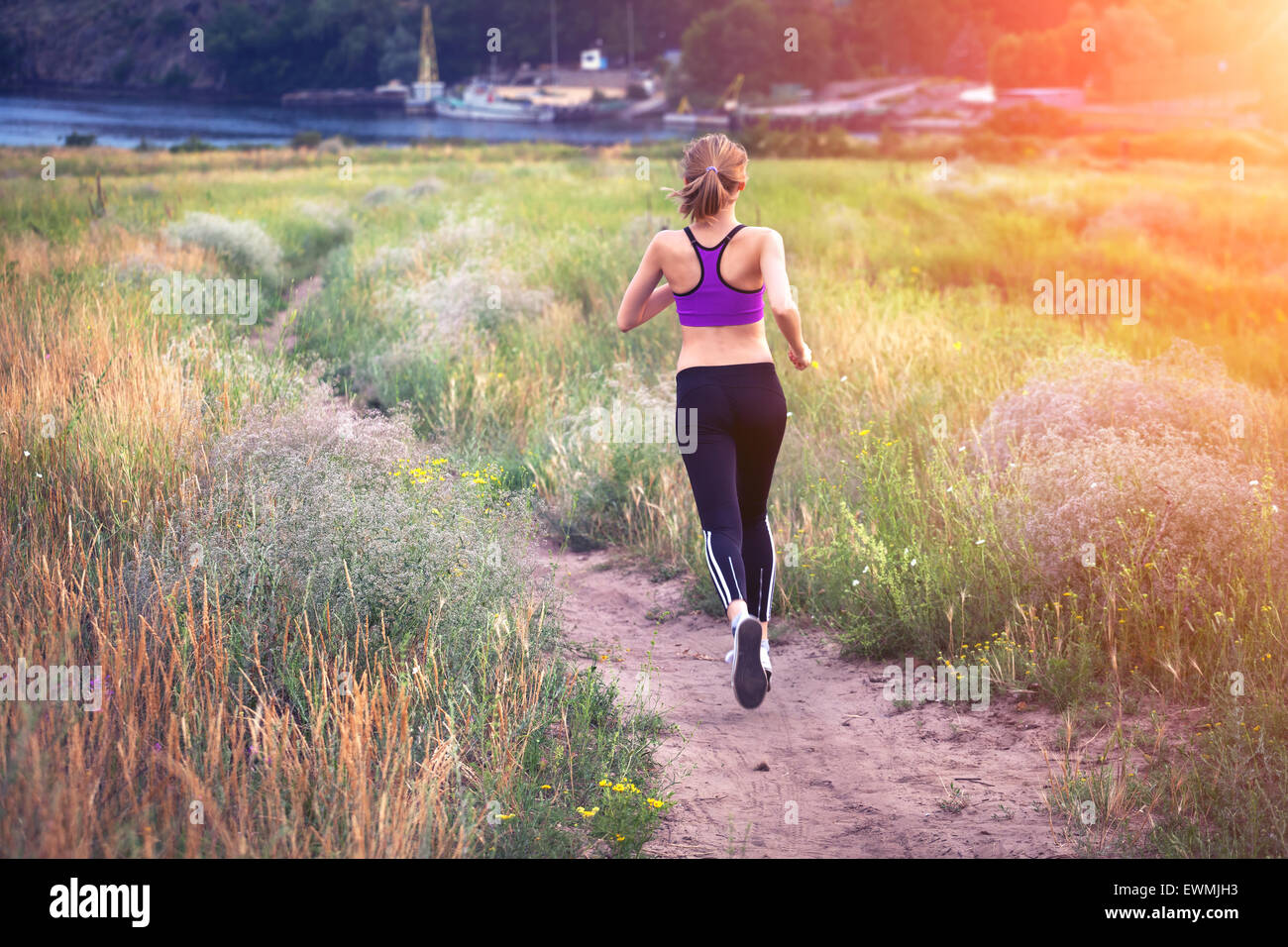 Young woman running on a rural road at sunset in summer field. Lifestyle sports background Stock Photo