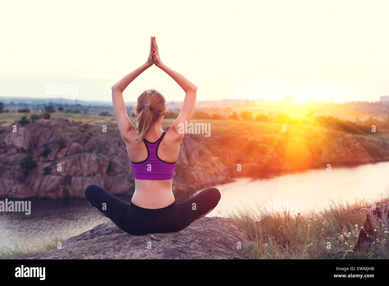 Young woman practicing yoga on the hill at sunset near the river. Stock Photo