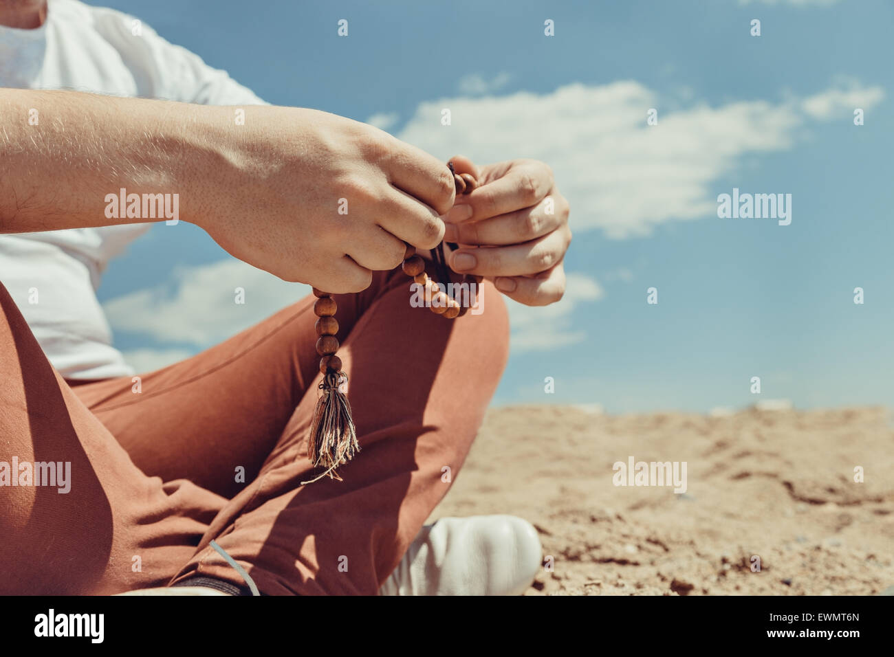 Young hipster man holds a rosary in his hands, sitting on the ground in a sunny summer day Stock Photo