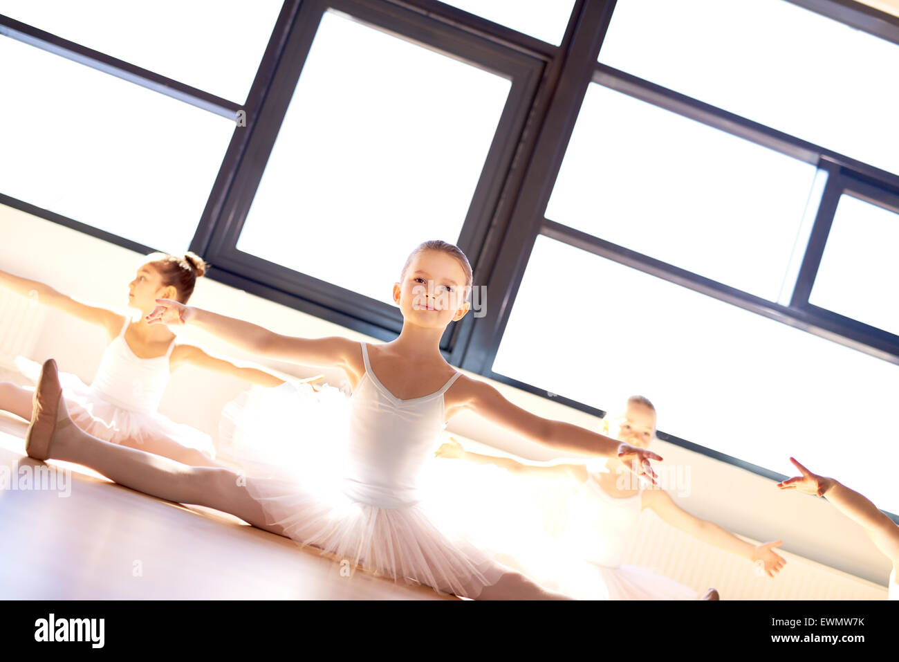 Pretty little ballerina in ballet class sitting on the wooden floor in a bright sunlit dance studio practising her poses , low a Stock Photo
