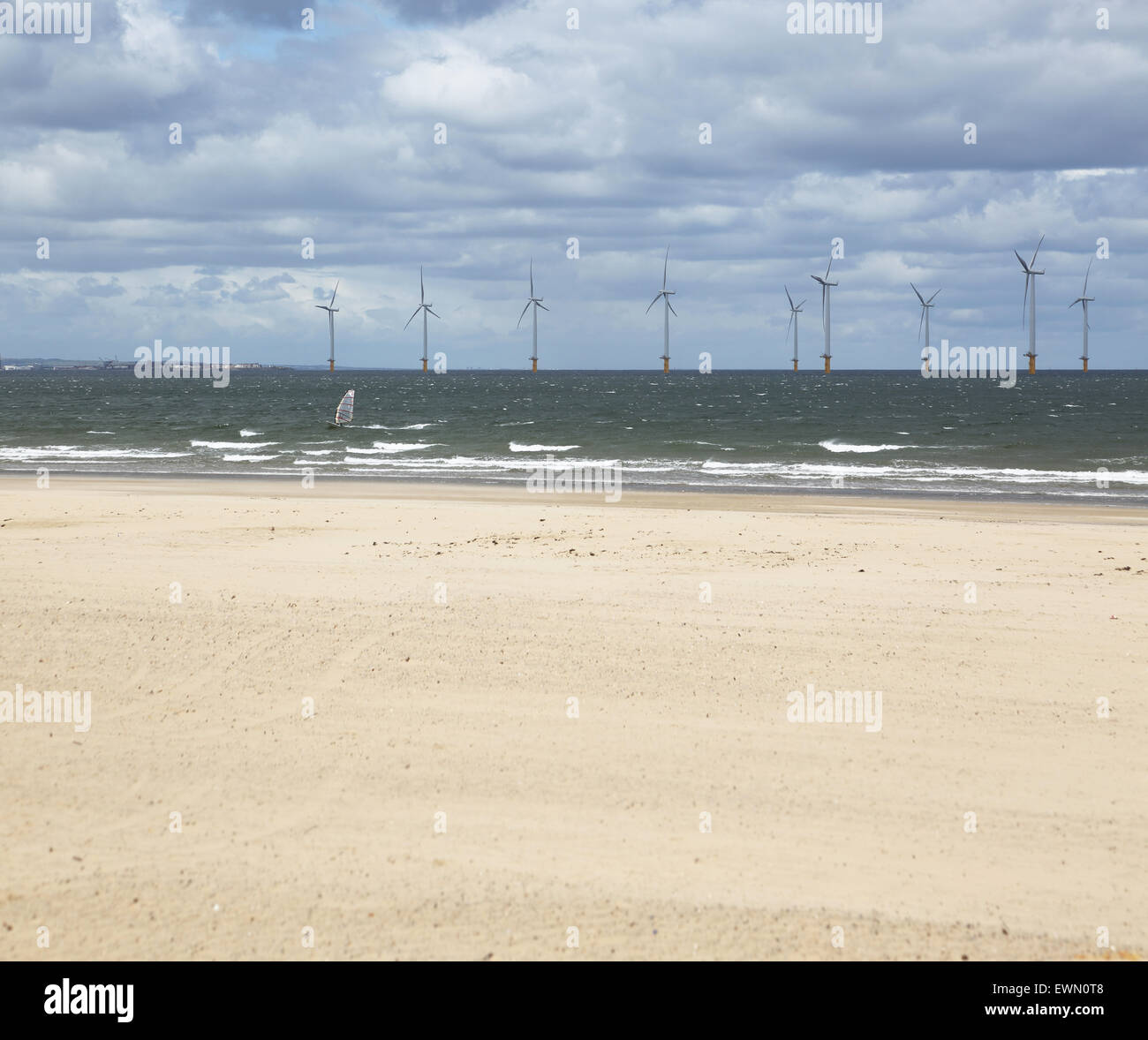 A windsurfer sails in front of an offshore wind farm in the River Tees estuary photographed from Redcar beach. Stock Photo