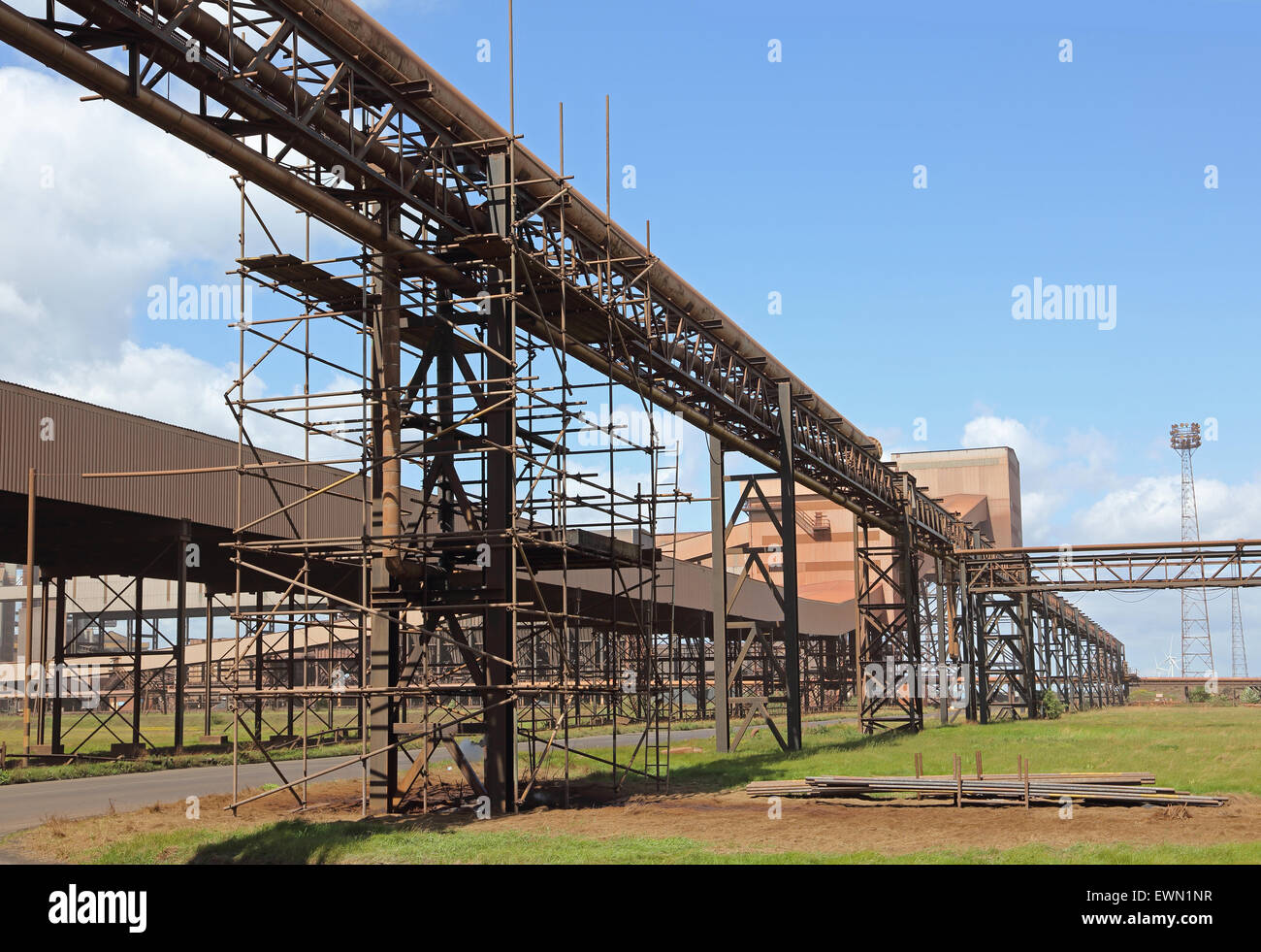 Scaffolding surrounds pipe gantries and conveyor belt housings at the