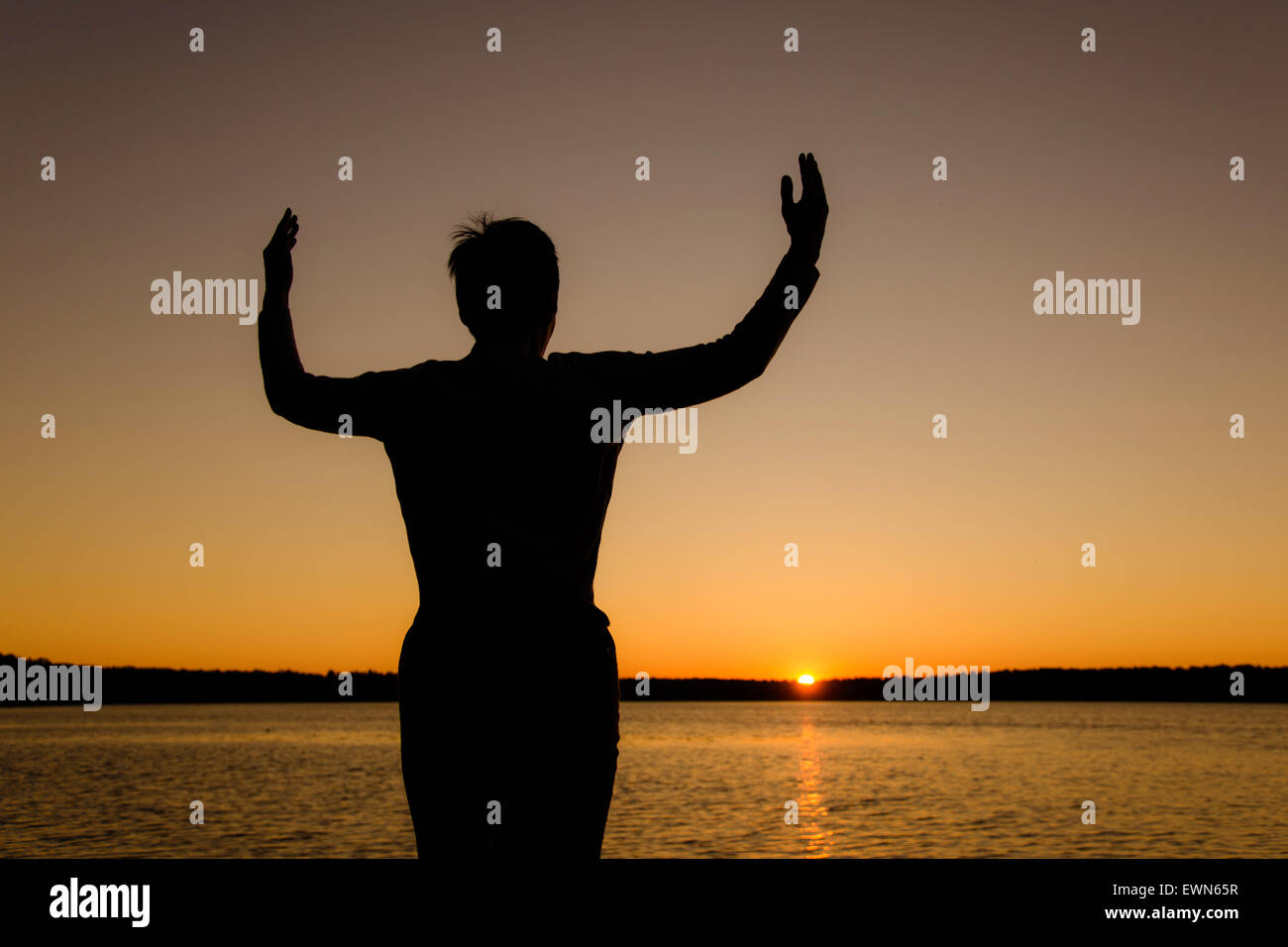 Happy woman with hands up at sunset or sunrise Stock Photo