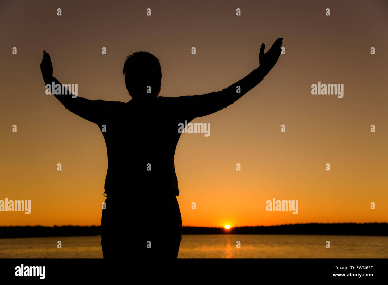 Happy woman with hands up at sunset or sunrise Stock Photo