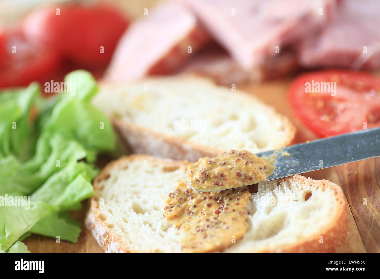 Putting wholegrain mustard on bread to make a ham sandwich Stock Photo