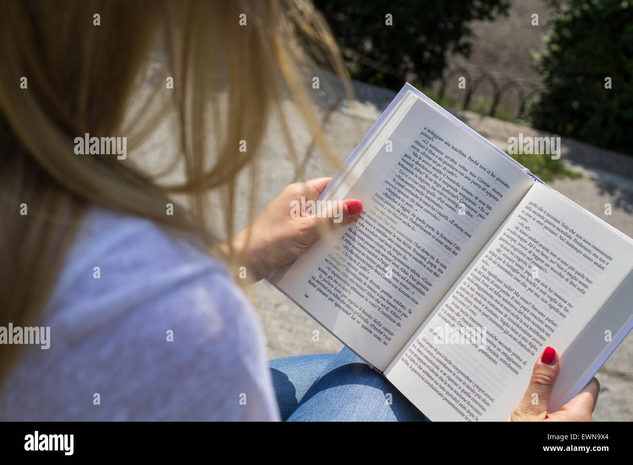 Portrait of a female blonde student reading a book outside in the city. Stock Photo