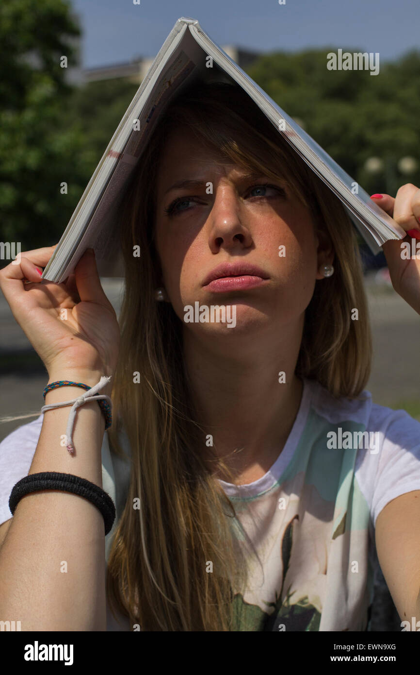 Bored female student outside with a book over her head during a hot sunny day in the summer Stock Photo