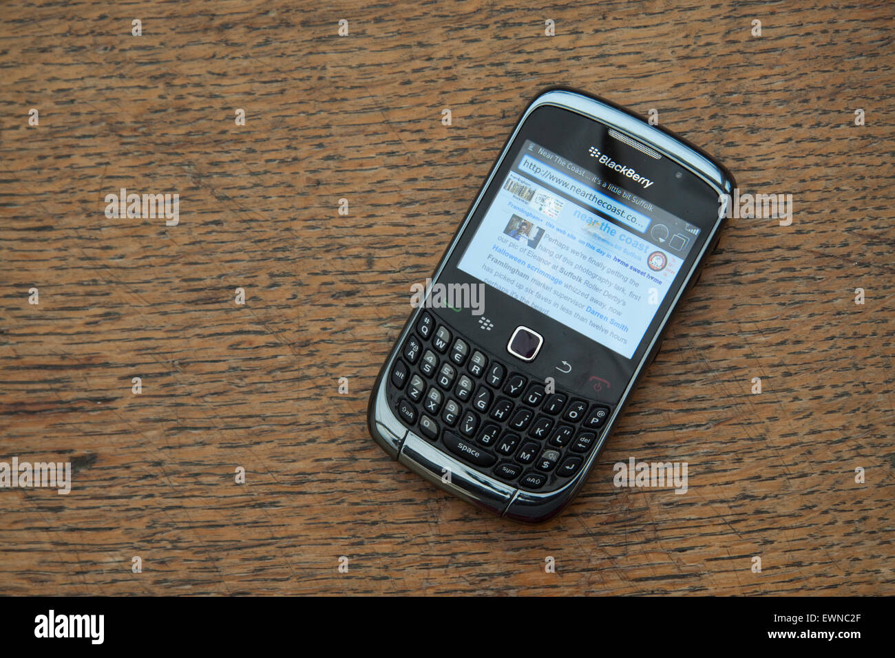 On a grained wooden surface a Blackberry Curve 8320 smartphone showing a pale blue web site in the browser Stock Photo