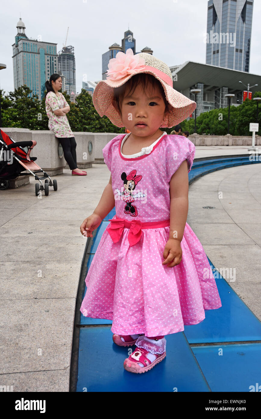 Little girl with pink dress and hat Fountain with people and children on People's Square Municipal Government Building Shanghai Municipality China skyline city Stock Photo