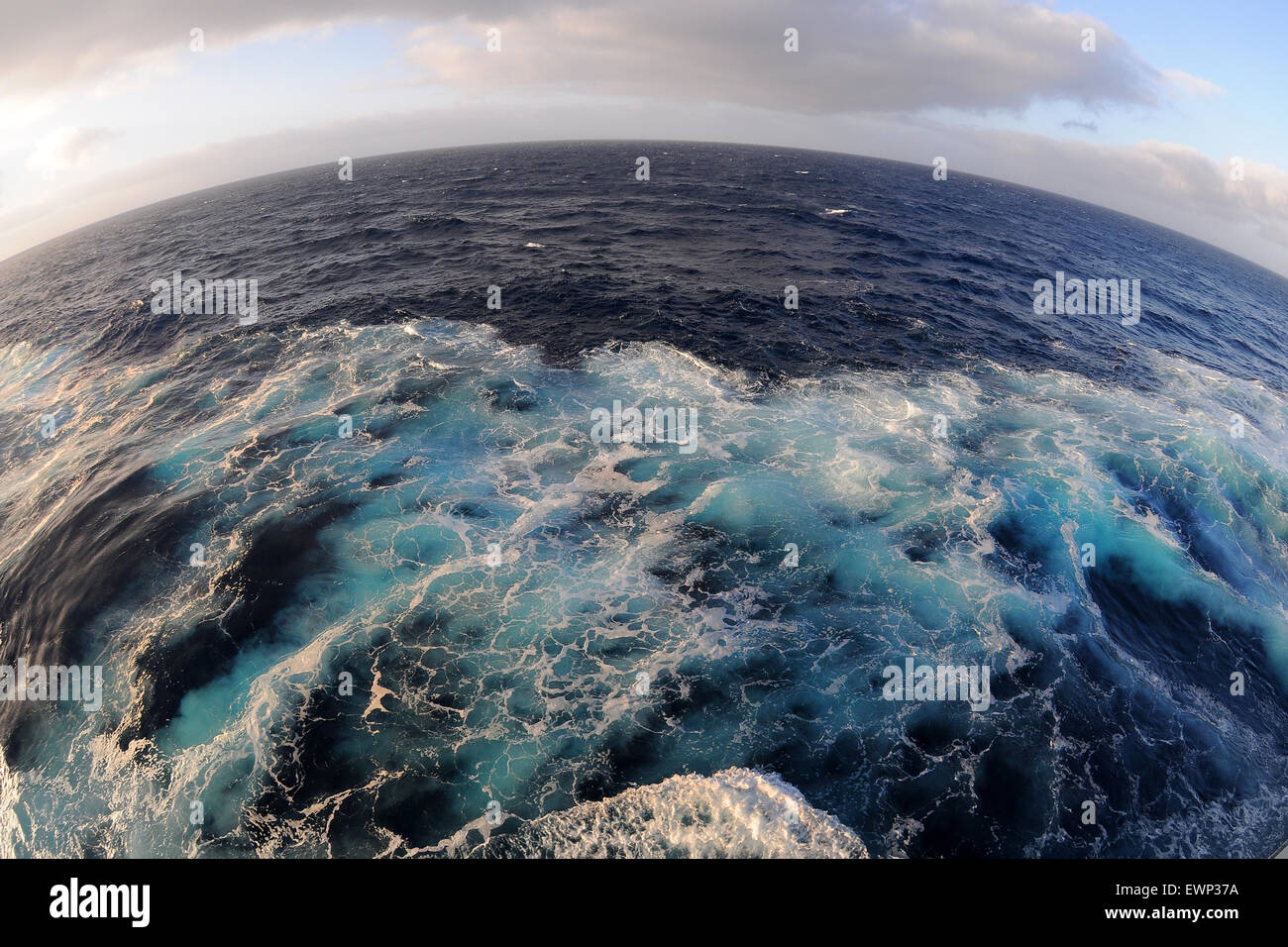 A fish eye view of blue waves in the sea at sunset from the side of a cruise ship. Stock Photo