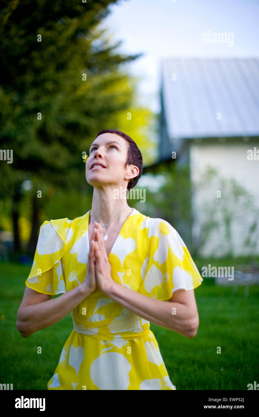 Adult woman in yellow dress praying outside in her front yard Stock Photo