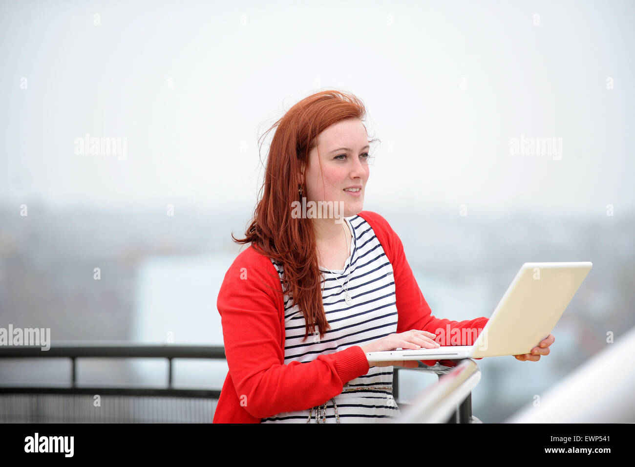 A red headed girl works on the Internet using a wireless laptop in an ...