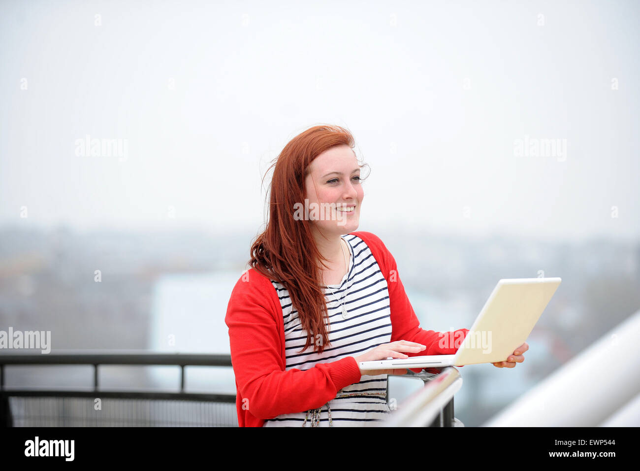 A red headed girl works on the Internet using a wireless laptop in an ...