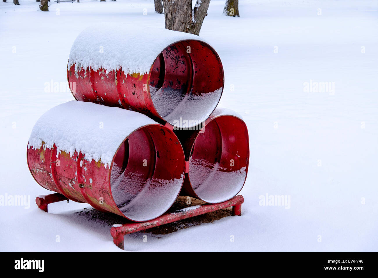 Three red barrels welded together for climbing in a park playground. Winter, snow. Stock Photo