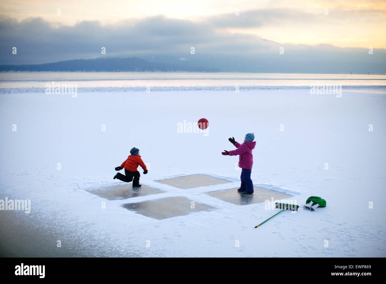 Boy, age 6 and girl, age 10 playing a game of four square on a frozen lake in the middle of winter. Stock Photo
