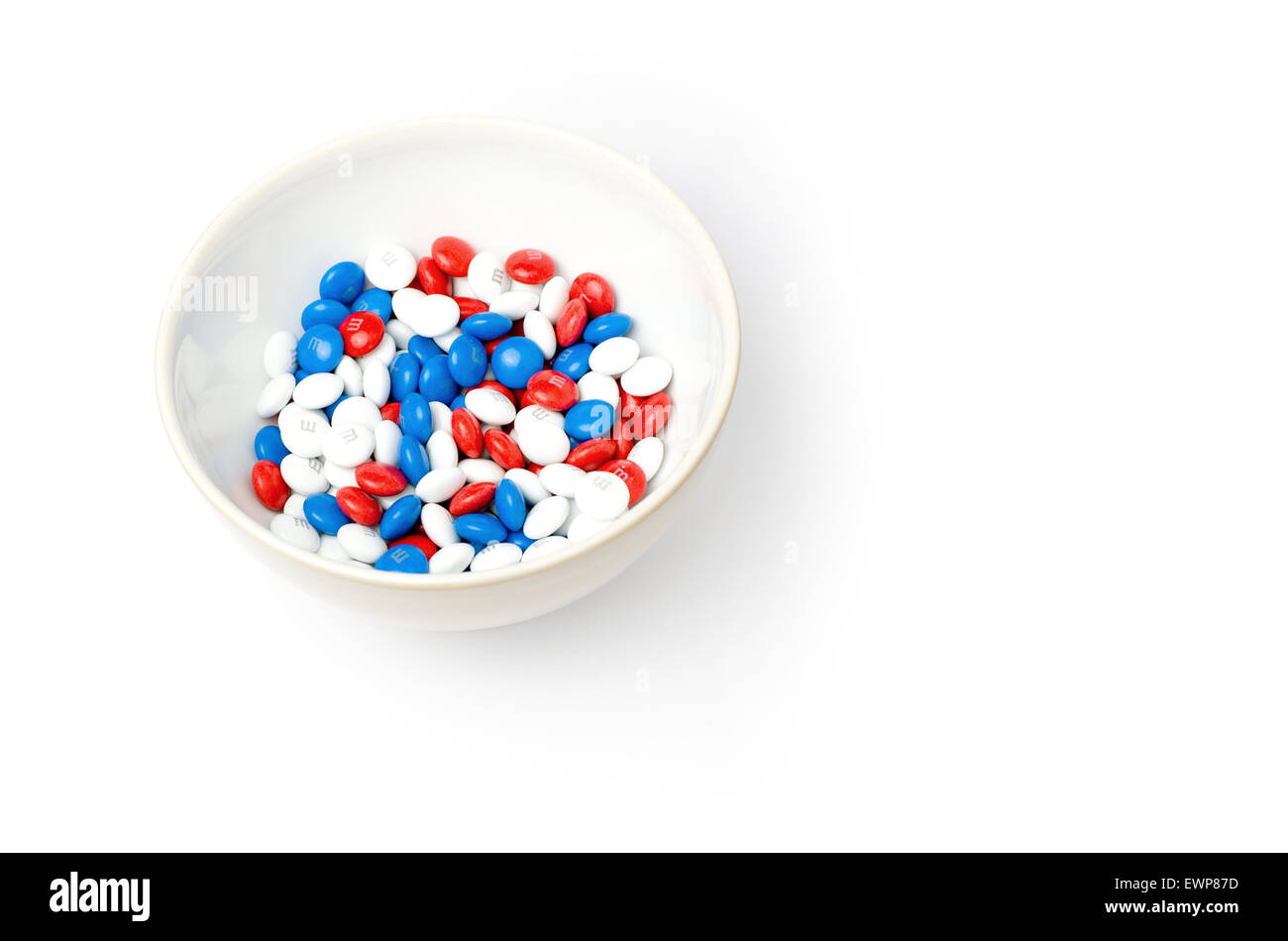 Red, white and blue M&Ms in a white bowl on a white background. Ms