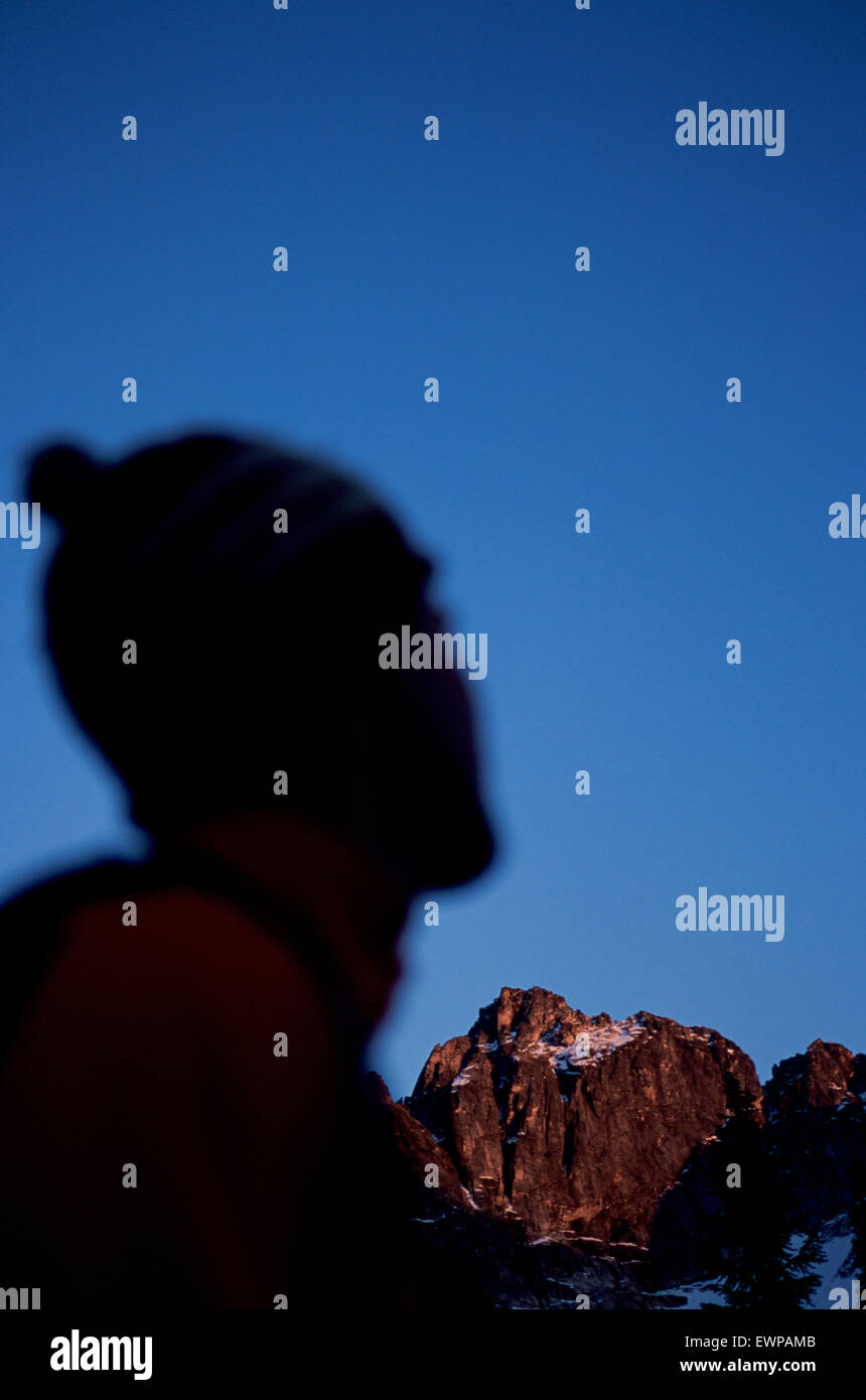 A silhouetted hiker pauses to watch the last rays of sun hit a mountain peak in the Valhalla Range, British Columbia, Canada. Stock Photo