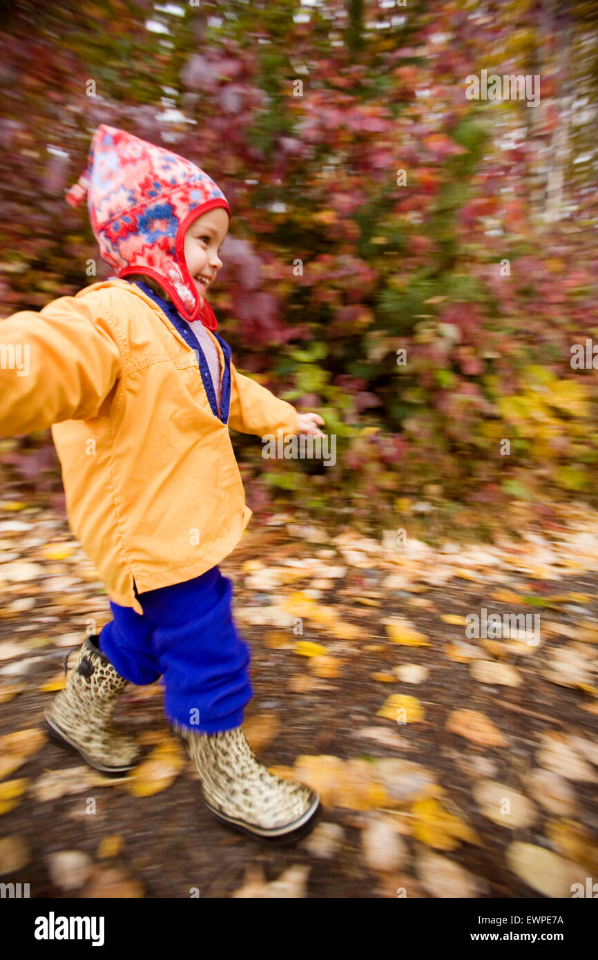 Little girl with hat and raincoat running down trail in falltime Stock