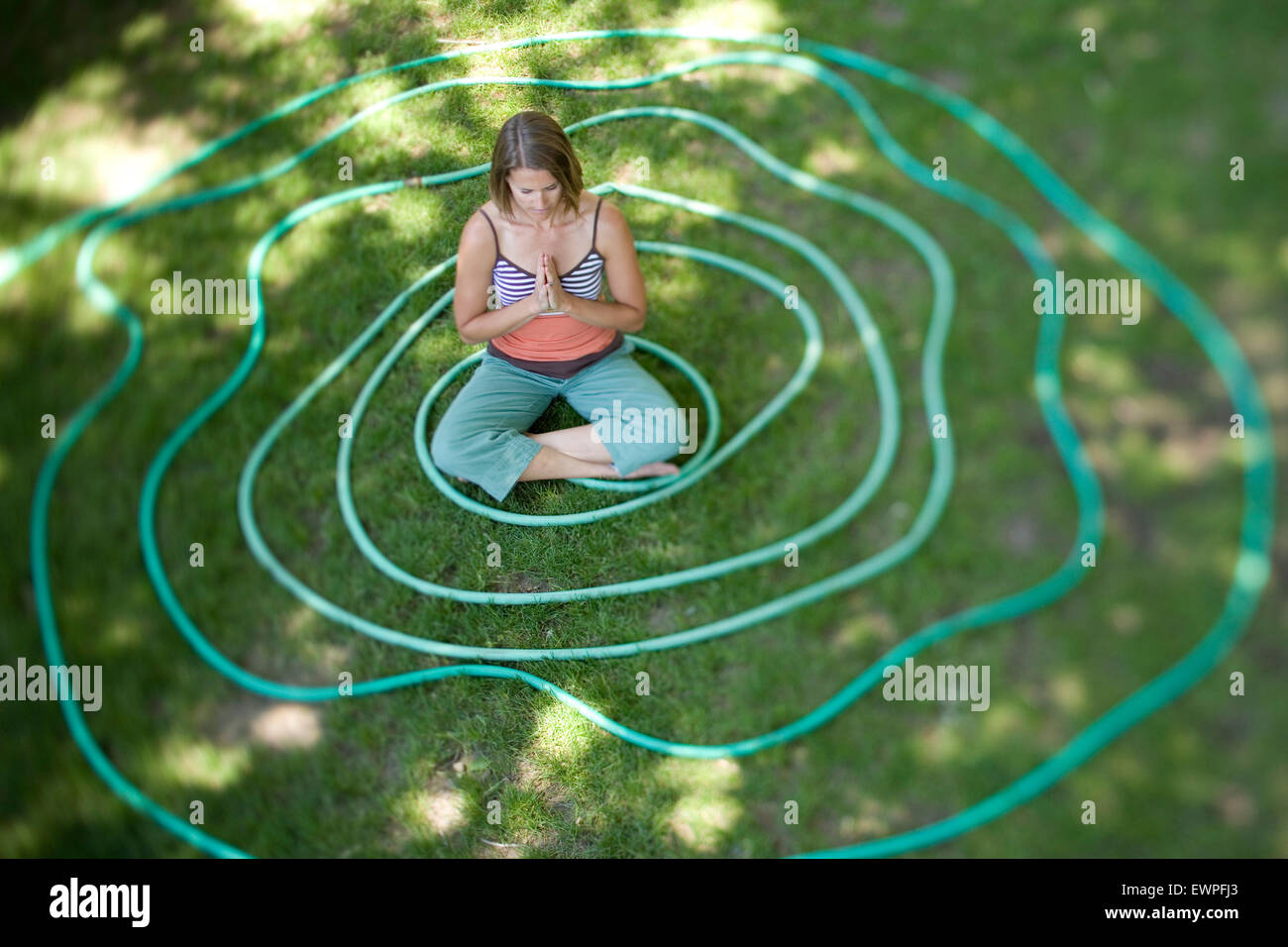A woman meditates in the middle of a coiled garden hose in Hailey, Idaho. Stock Photo