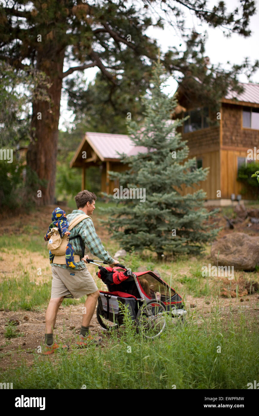 Father pushing baby jogger with kids while wearing another child on his  back Stock Photo - Alamy
