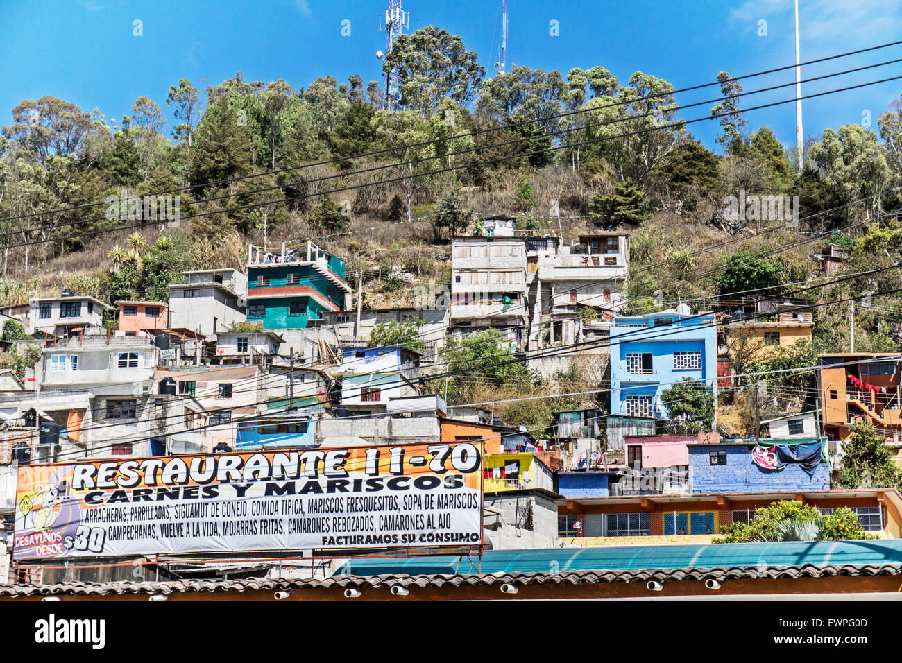 tightly clustered middle class homes cling to steep hillside above restaurant sign at street level in San Cristobal de las Casas Stock Photo