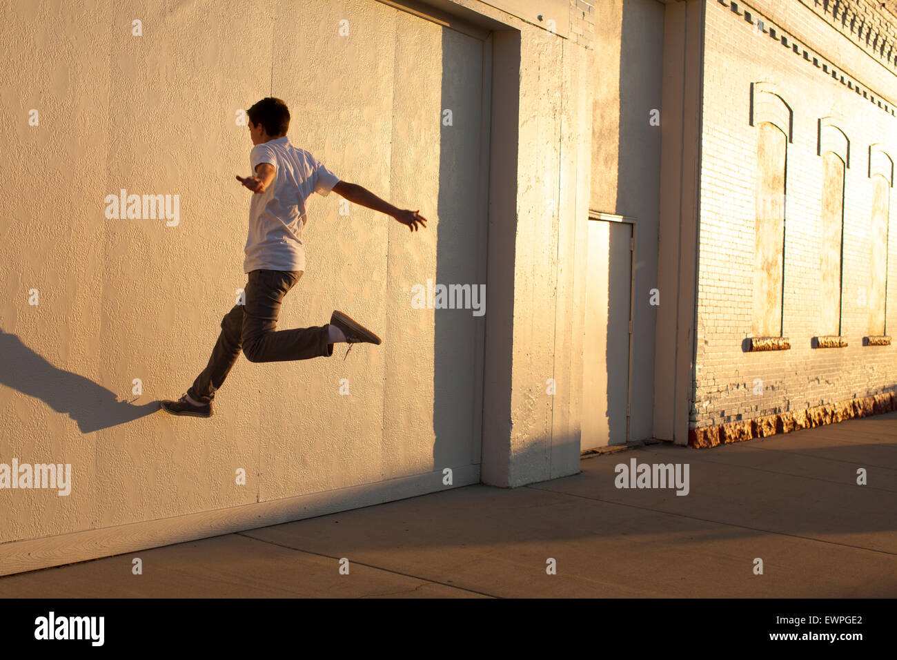 A teenage boy playing with his shadow on the side of a white building. Stock Photo