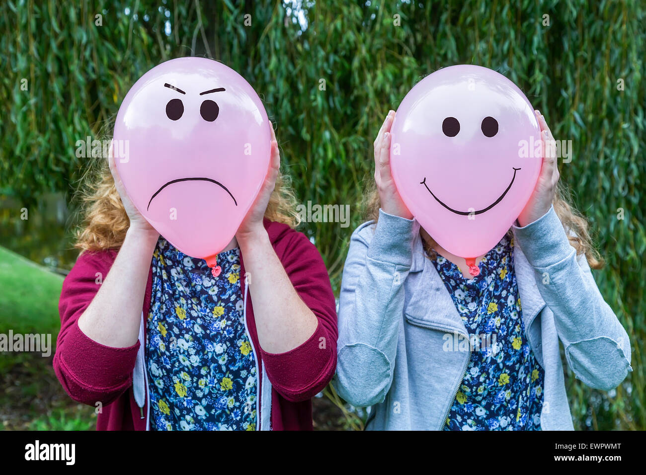 Two teenage girls holding balloons with smiling and angry facial expressions outdoors Stock Photo