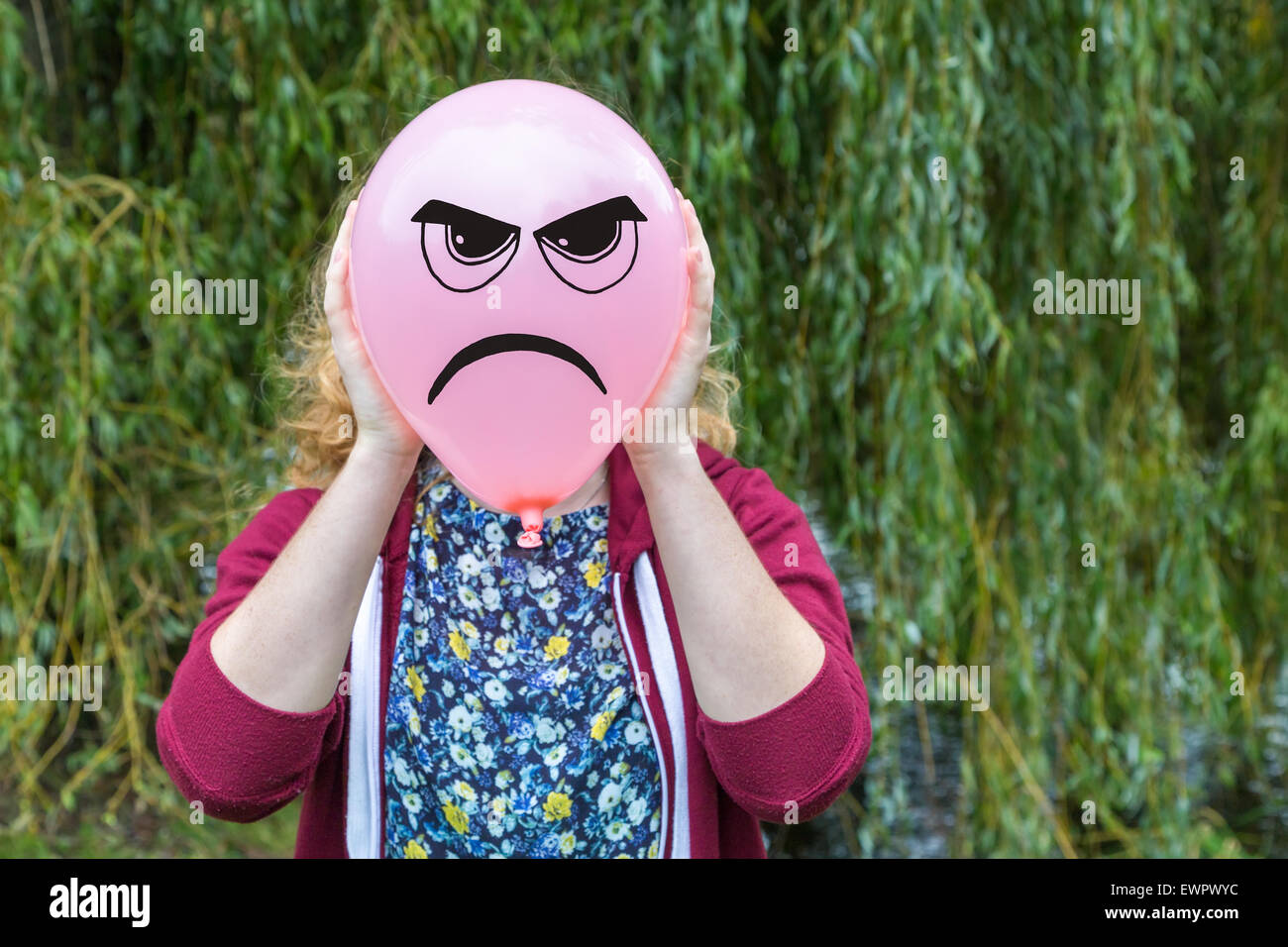 Teenage girl holding balloon with angry face as expression in nature Stock Photo