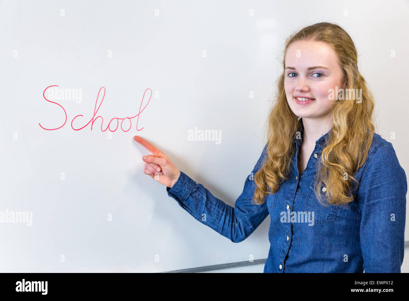 Caucasian teenage girl pointing at word School written on white board in classroom Stock Photo