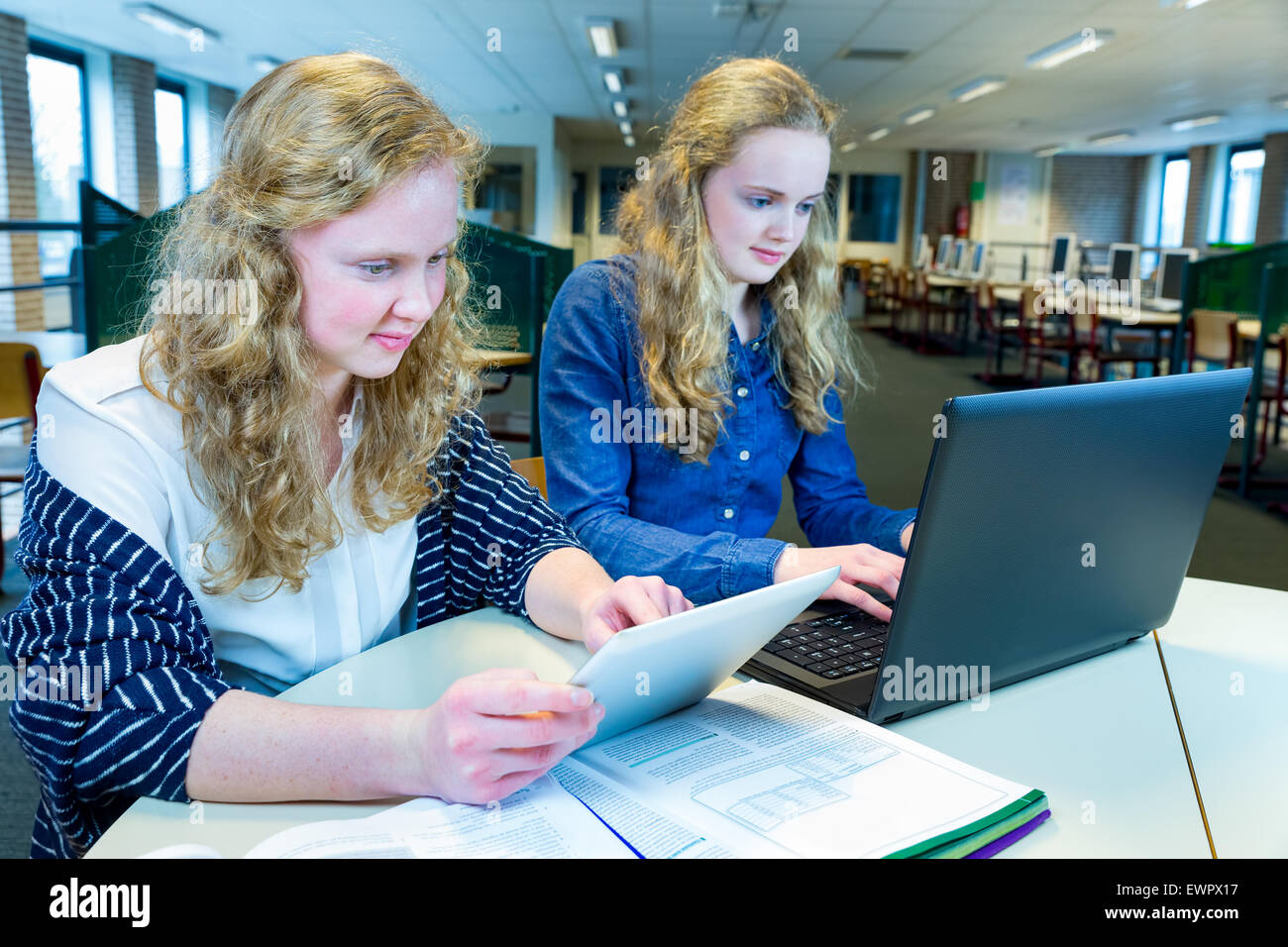 Two caucasian sisters with long hair working on computer and tablet in ...