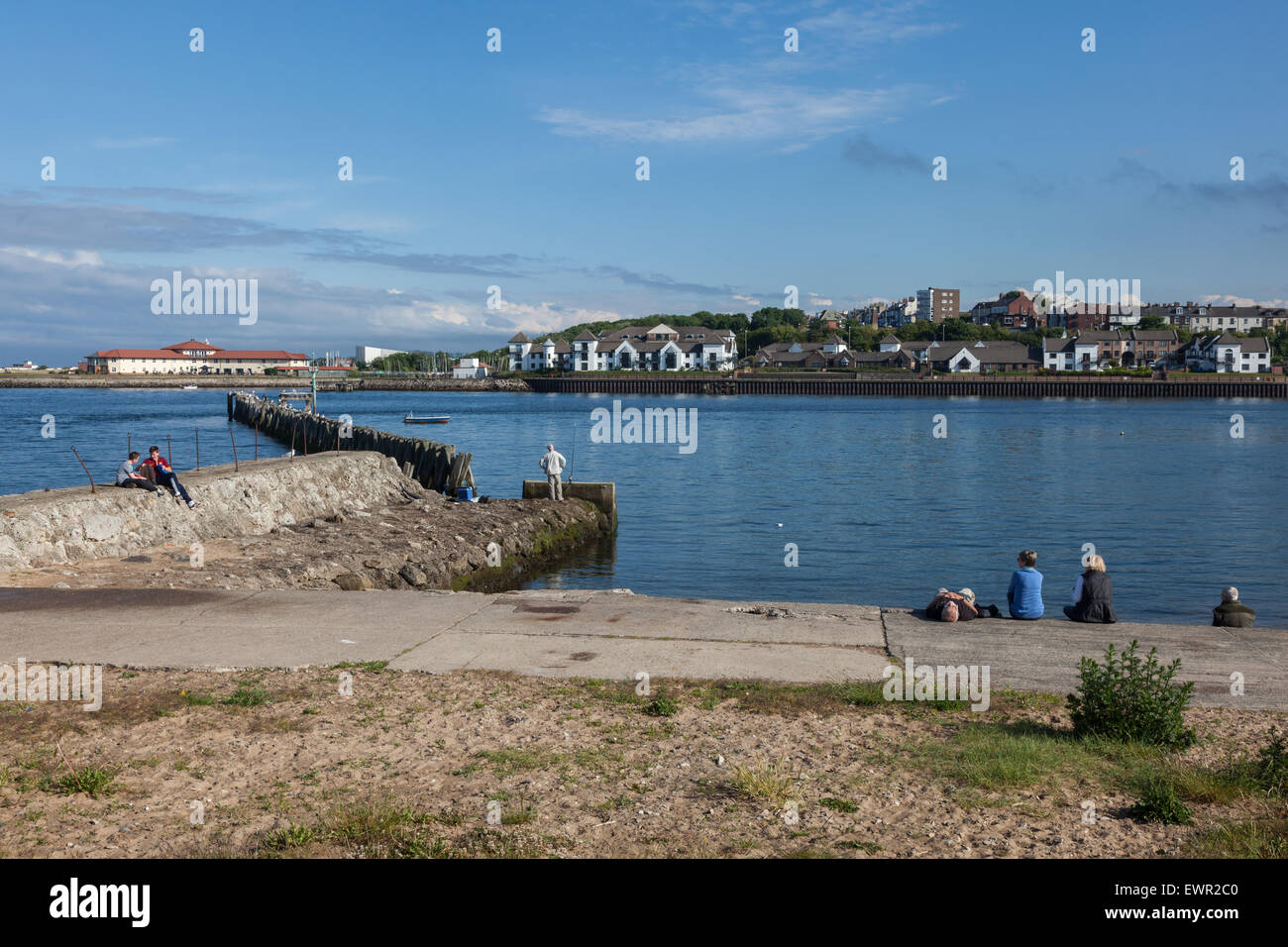 A family relaxes by the side of the River Tyne, two teenage boys sit on a pier and talk while an angler waits for his catch, North Shiields. UK Stock Photo