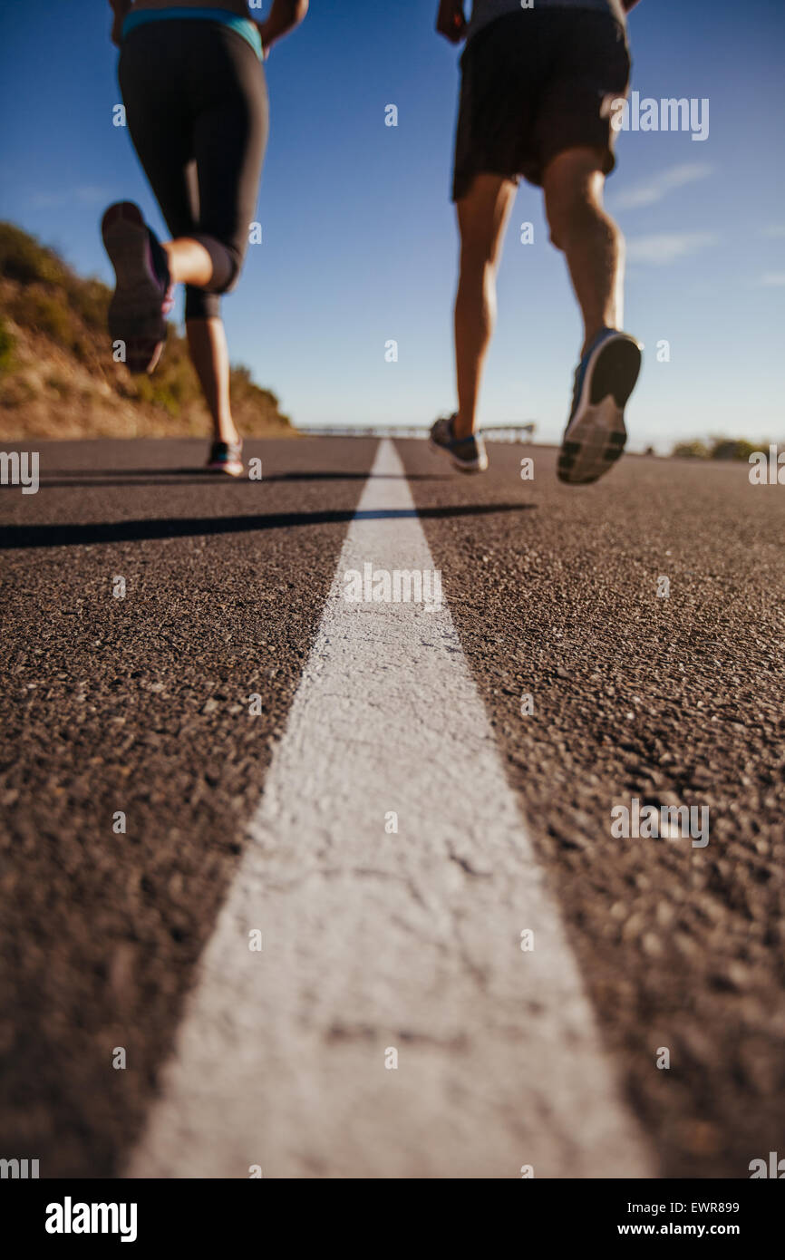 Cropped shot of two people running on road. Athletes training on country road. Low angle shot with focus on road. Stock Photo