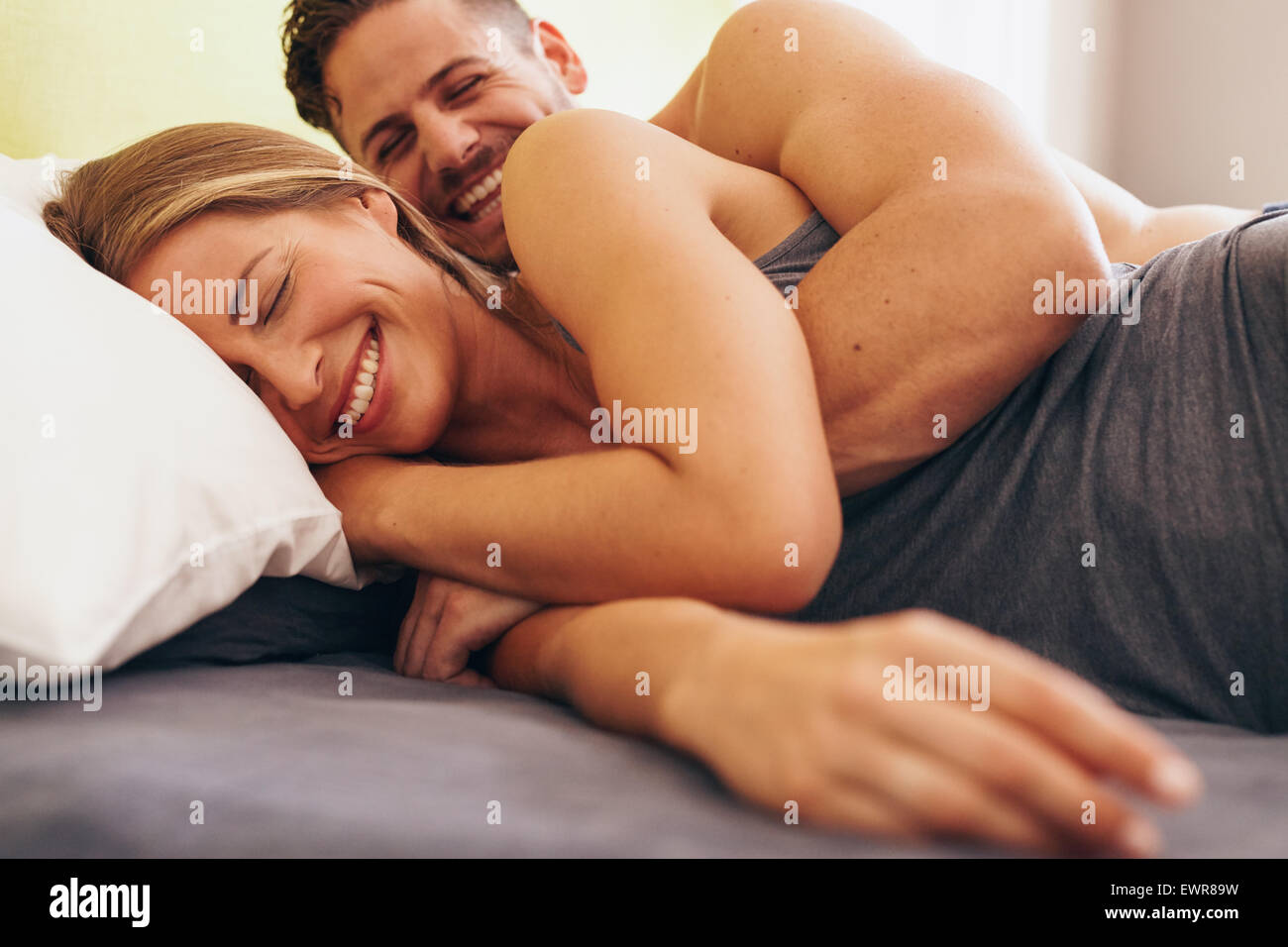 Image of cute young couple in love lying on bed. Man waking up his wife in morning. Stock Photo