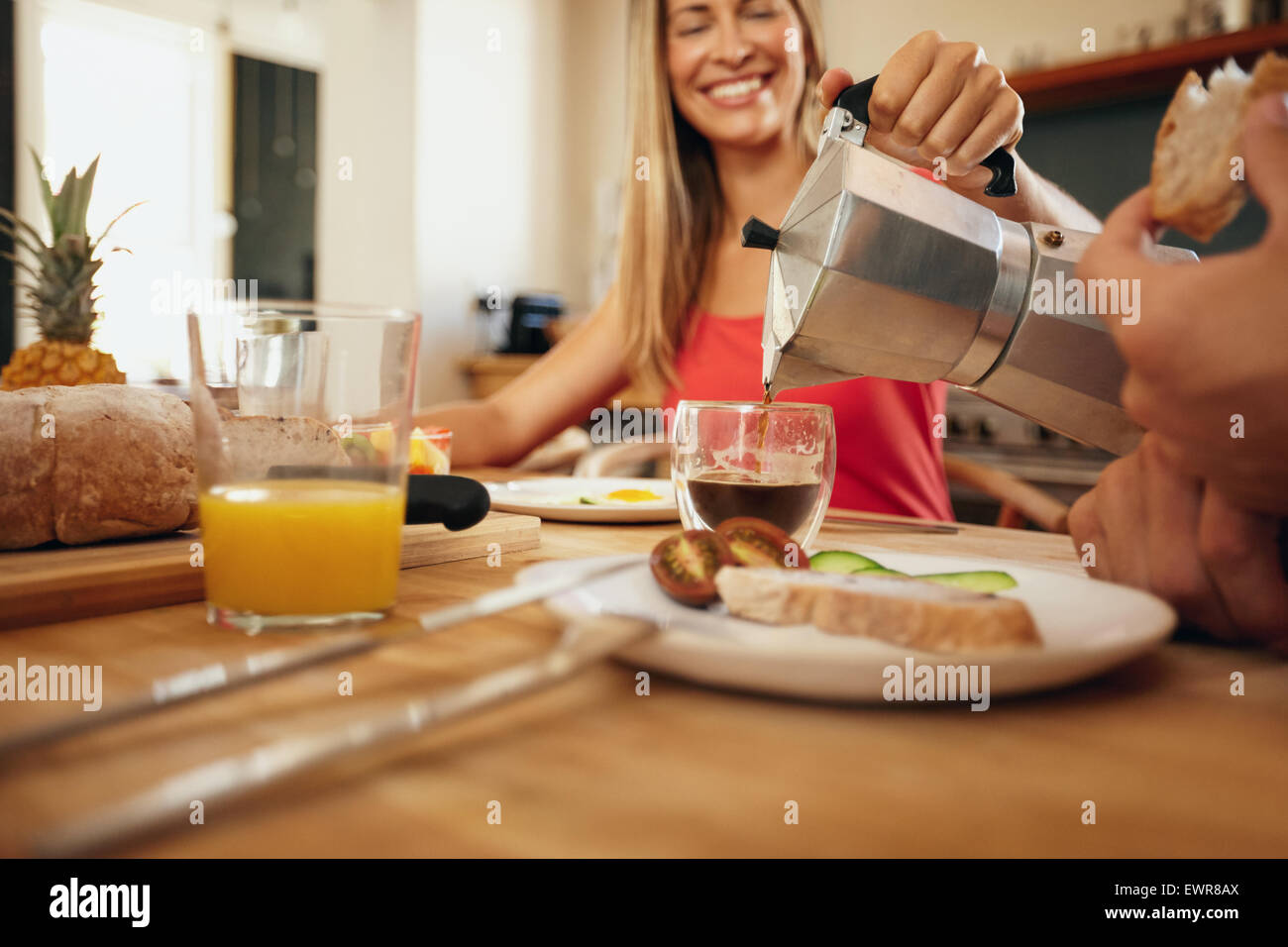 Indoor shot of woman pouring coffee in to a cup. Woman smiling while serving breakfast to man in kitchen at home. Young couple e Stock Photo