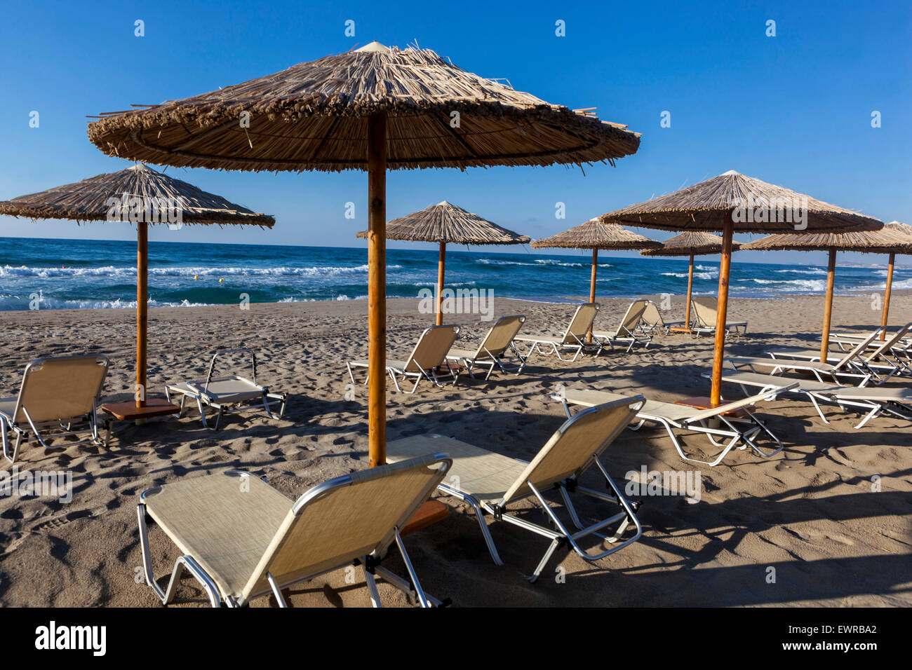 Straw beach umbrellas and sun loungers on the empty beach of Rethymno, Crete beach Greece Europe Stock Photo