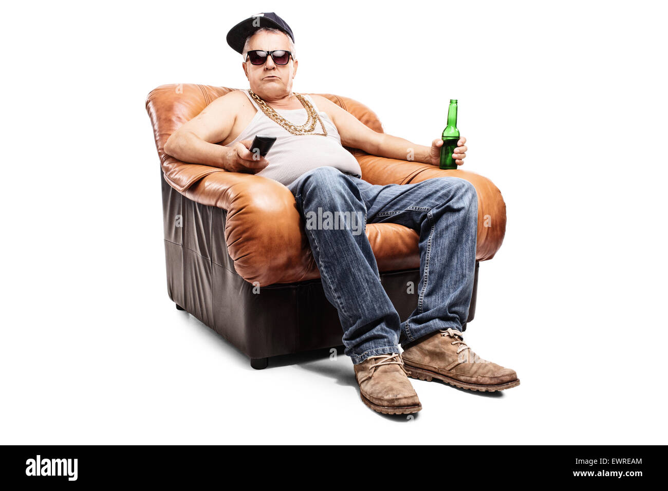 Senior man in a hip-hop outfit sitting in an armchair and holding a remote control isolated on white background Stock Photo