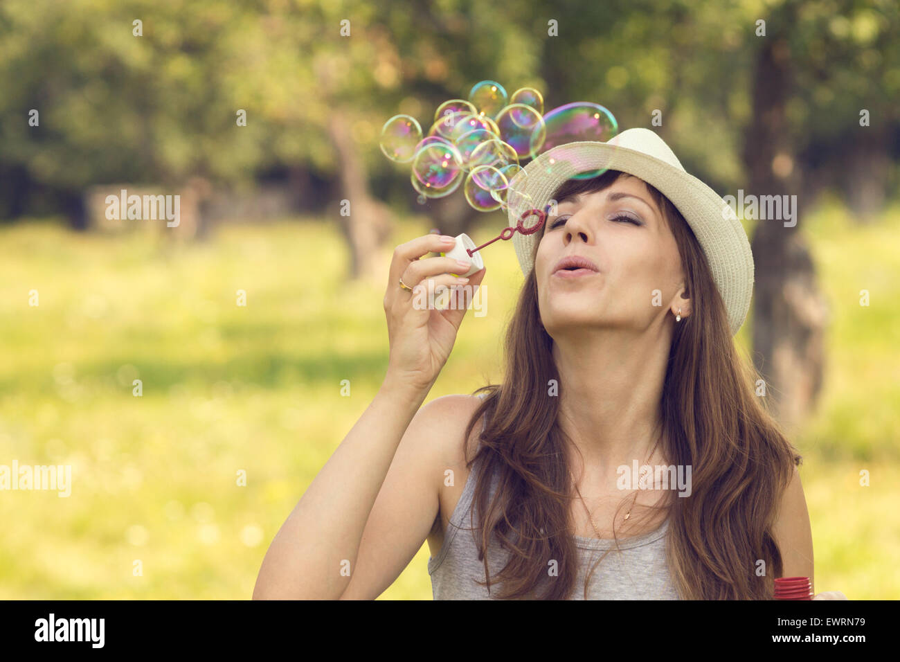Young pretty caucasian woman having fun with blowing bubbles in summer park. Warm color toned image Stock Photo
