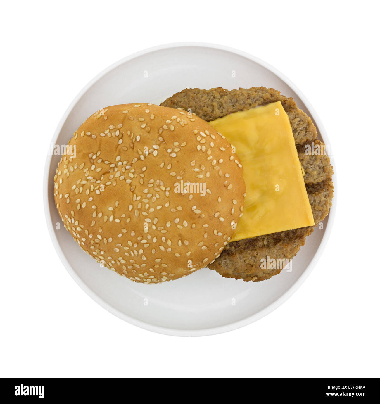 Top view of a microwaved cheeseburger with sesame seed bun on a small plate atop a white background. Stock Photo
