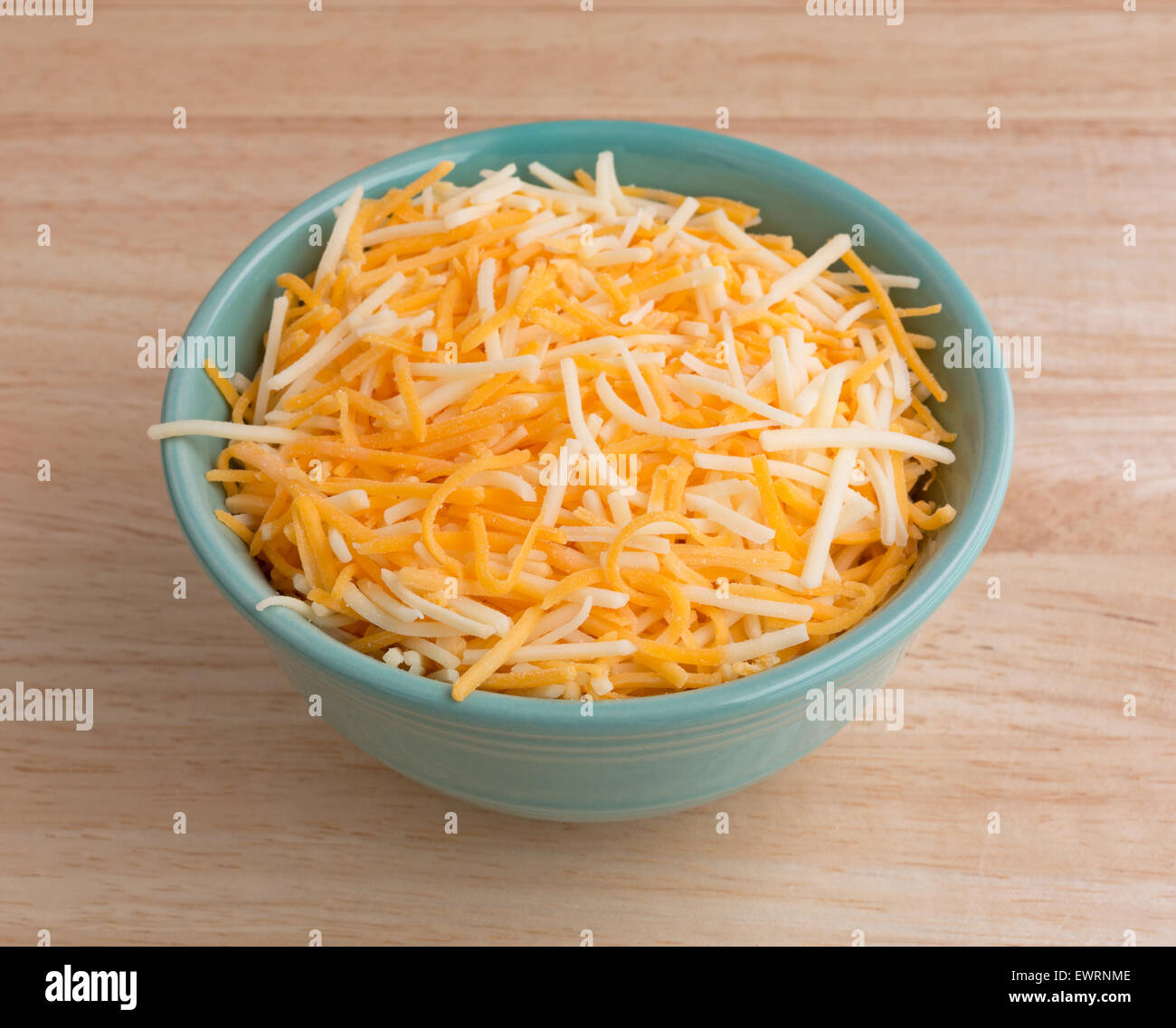 A small bowl filled with shredded white cheddar, sharp cheddar and mild cheddar cheeses atop a wood table top. Stock Photo