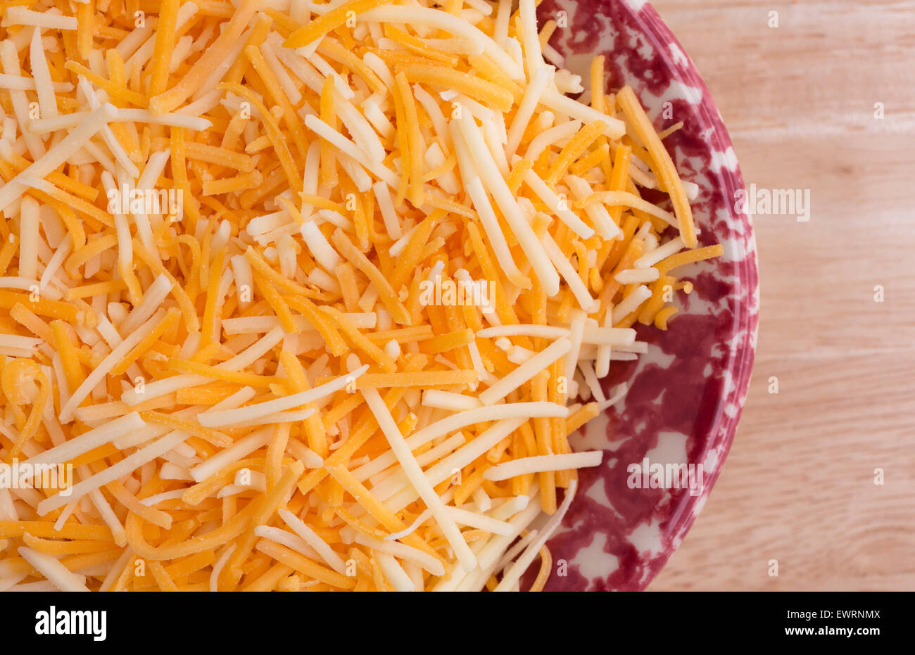 Top close view of a small colorful tray filled with shredded white cheddar, sharp cheddar and mild cheddar cheeses atop a wood t Stock Photo