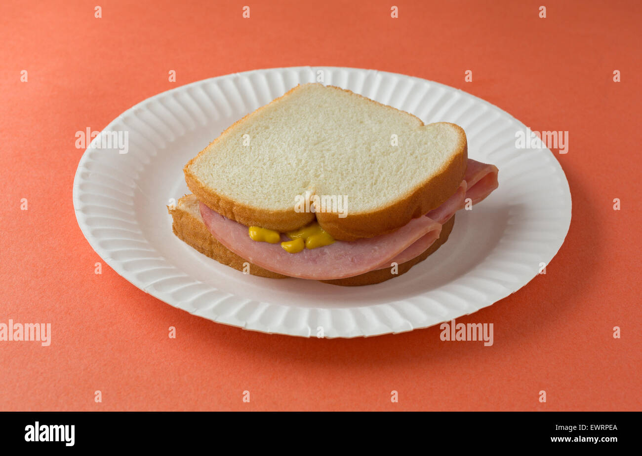 A honey ham sandwich with mustard on white bread upon a paper plate and